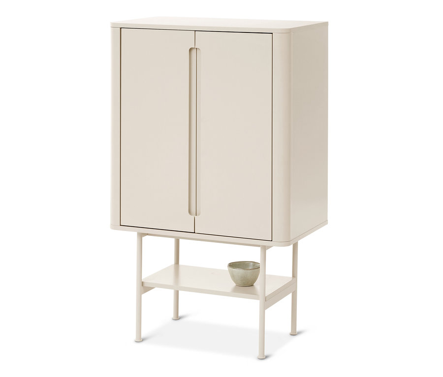 Une armoire couleur crème avec deux portes et des coins arrondis, reposant sur quatre pieds avec une étagère ouverte en dessous. Un petit bol de couleur claire est posé sur l'étagère.
