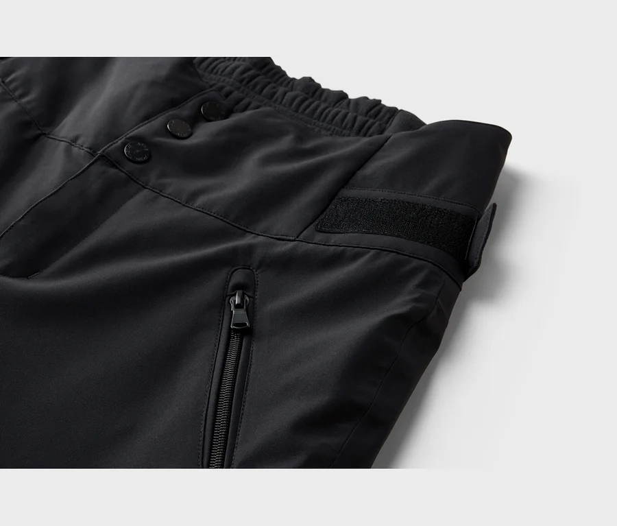 Gros plan d'un pantalon noir avec une taille élastique, trois boutons, une bande auto-agrippante et une poche zippée verticale.