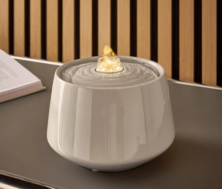 Fontaine en céramique grise avec de l'eau et une pierre éclairée sur une table grise.