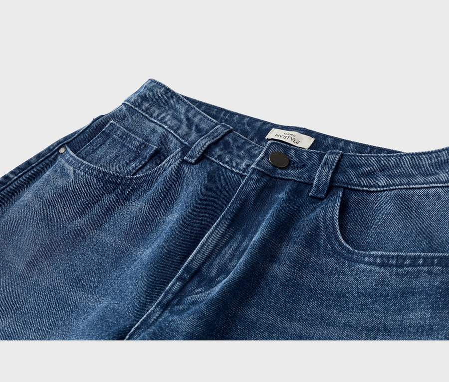 Jean en denim bleu, gros plan sur la partie supérieure avant avec poches avant, poche à monnaie, passants de ceinture, un bouton noir et une étiquette blanche « MYSTYLE ».