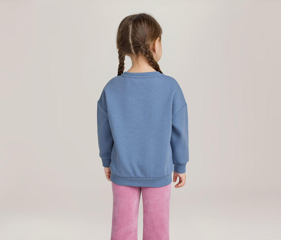 Enfant de dos, avec deux tresses, portant un sweat-shirt bleu et un pantalon en velours côtelé rose.