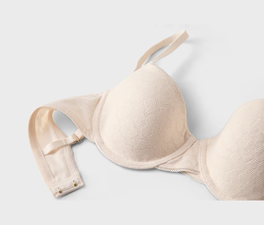 Soutien-gorge beige clair avec un motif texturé subtil, montrant un bonnet, une bretelle réglable et la fermeture à agrafes.