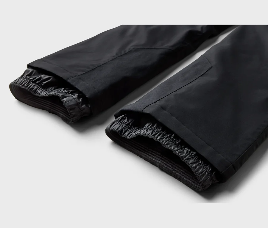 Deux bas de pantalon noirs avec des poignets intérieurs élastiques, probablement des guêtres de neige, sur fond clair.