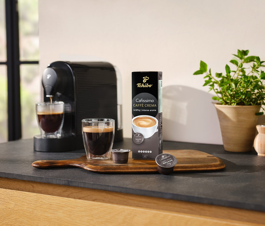 Machine à café préparant du café dans un verre à côté d'un paquet de Cafissimo Caffè Crema Kräftig (corsé) – 10 capsules.