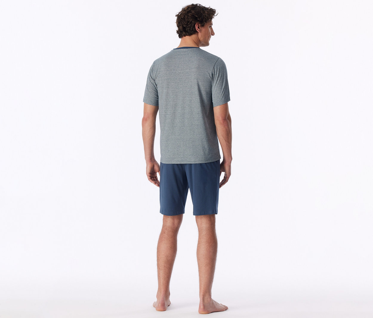 Homme de dos, portant un t-shirt gris et un short bleu, pieds nus.