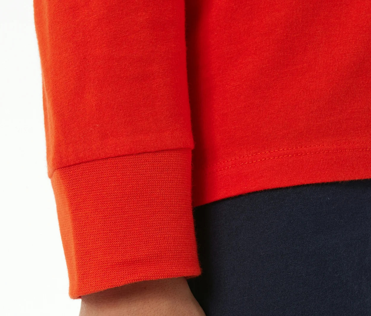 Gros plan sur un enfant portant un pyjama enfant SCHIESSER rouge avec des poignets. La manche rouge avec poignet côtelé et une partie du pantalon bleu foncé sont visibles.