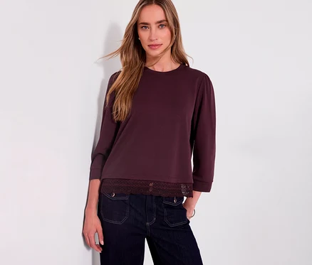 Femme portant un t-shirt en jersey 3/4 rouge Street One avec bordure en dentelle et un jean foncé, appuyée contre un mur blanc.