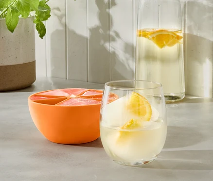 Un moule à glaçons XL orange à côté d'un verre avec une boisson et une bouteille d'eau.