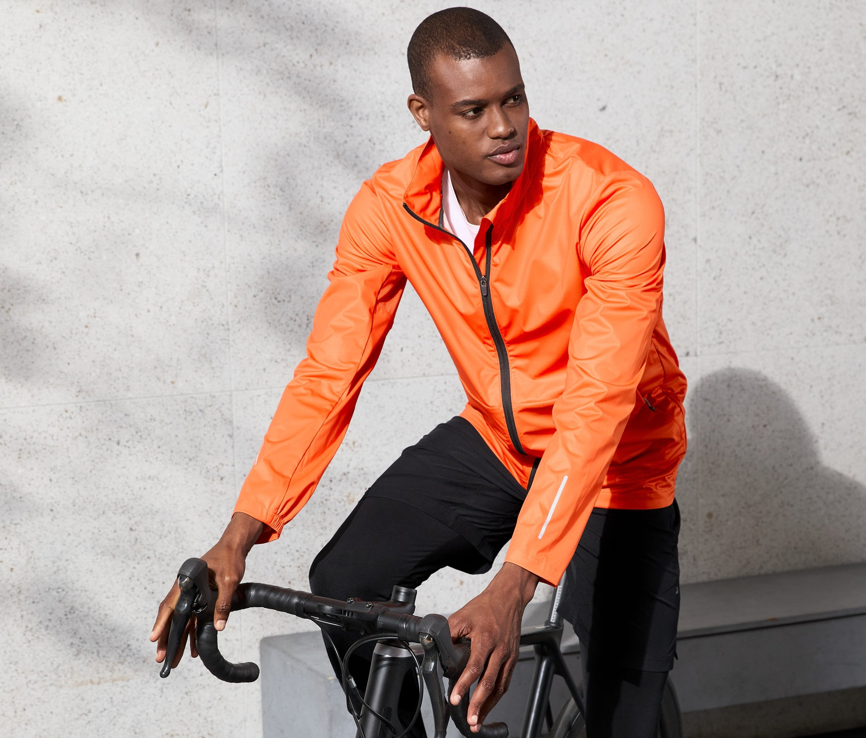 Un homme sur un vélo porte une veste fonctionnelle coupe-vent orange.