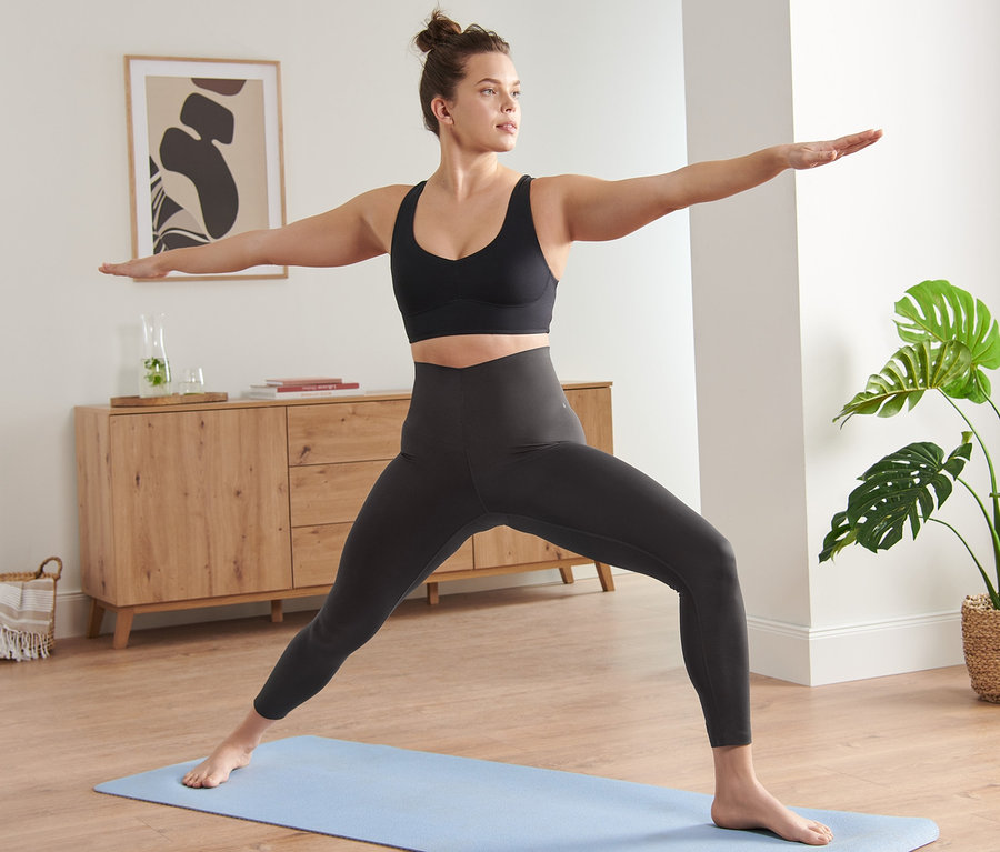 Femme en tenue de sport faisant du yoga sur un tapis bleu. Elle porte un legging de sport premium 7/8.
