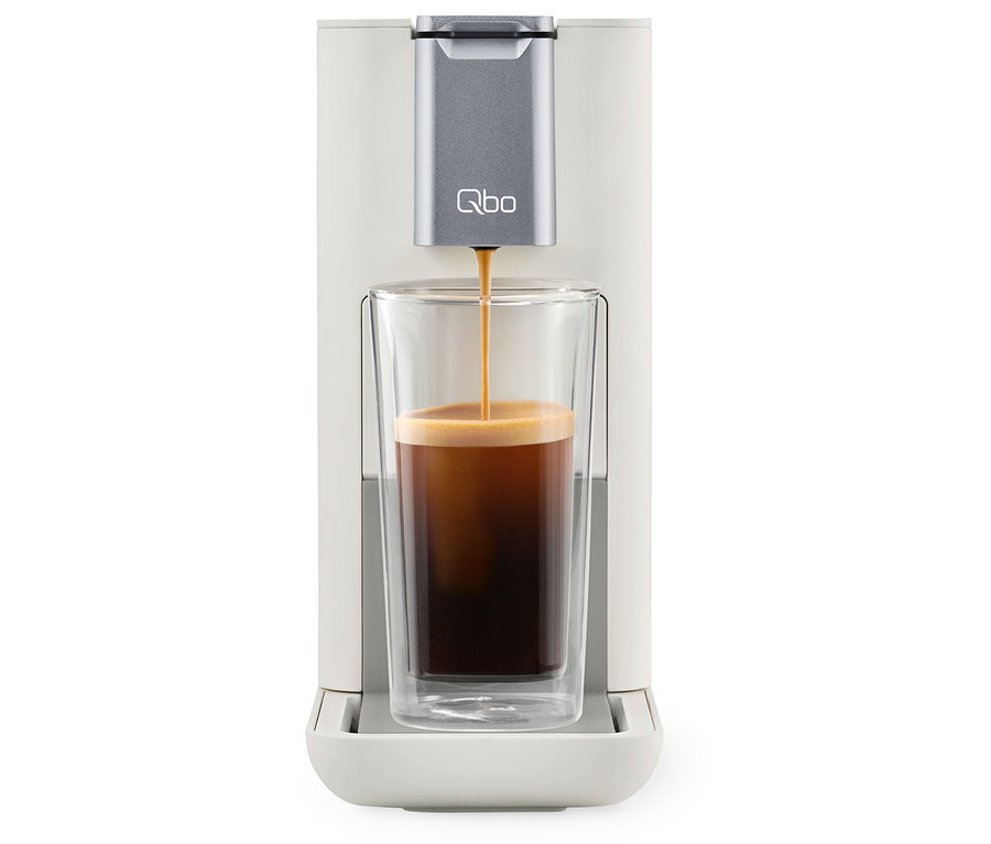 Du café est versé dans un verre à partir d'une machine à café Qbo ESSENTIAL Bright Sand.