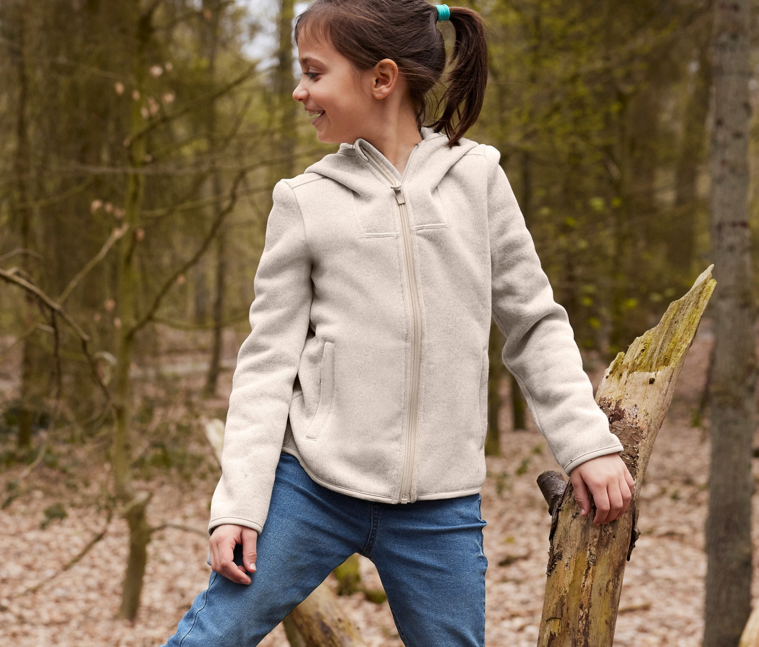 Un garçon est assis sur un arbre tombé et porte des bottes de pluie recyclables jaunes et un bonnet réversible marron, avec un pantalon de jogging en denim et une veste en maille polaire. Une fille se tient sur l'arbre, portant un jean et une veste en maille polaire.