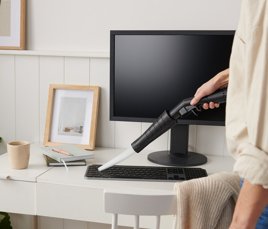 Une femme utilise un embout d'aspirateur sur un clavier d'ordinateur sur un bureau blanc.