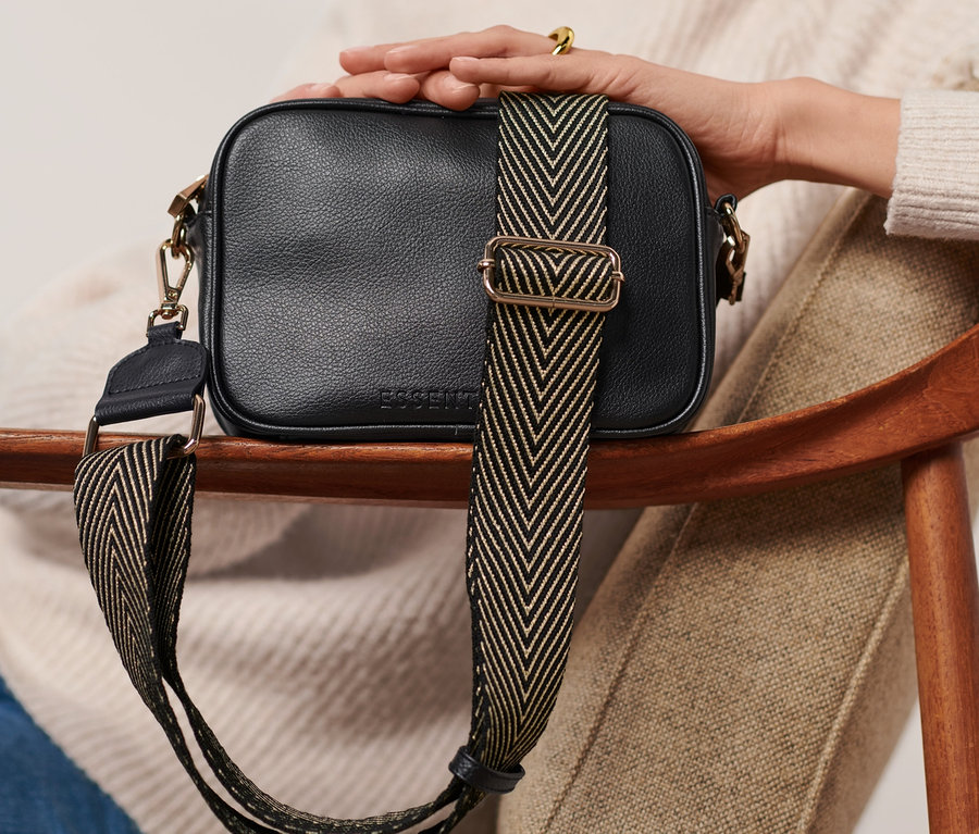 Femme assise tenant un sac à main noir avec une bandoulière de rechange.