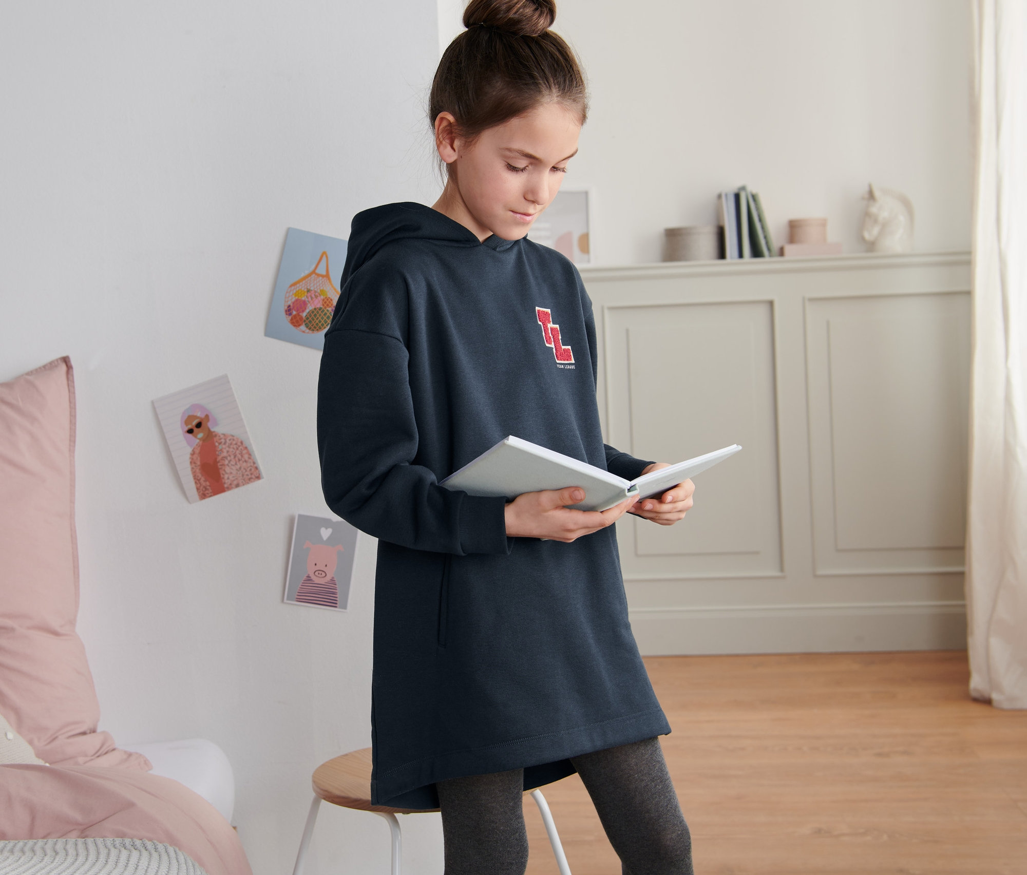 Une fille lit un livre et porte un sweat-shirt long à capuche bleu.