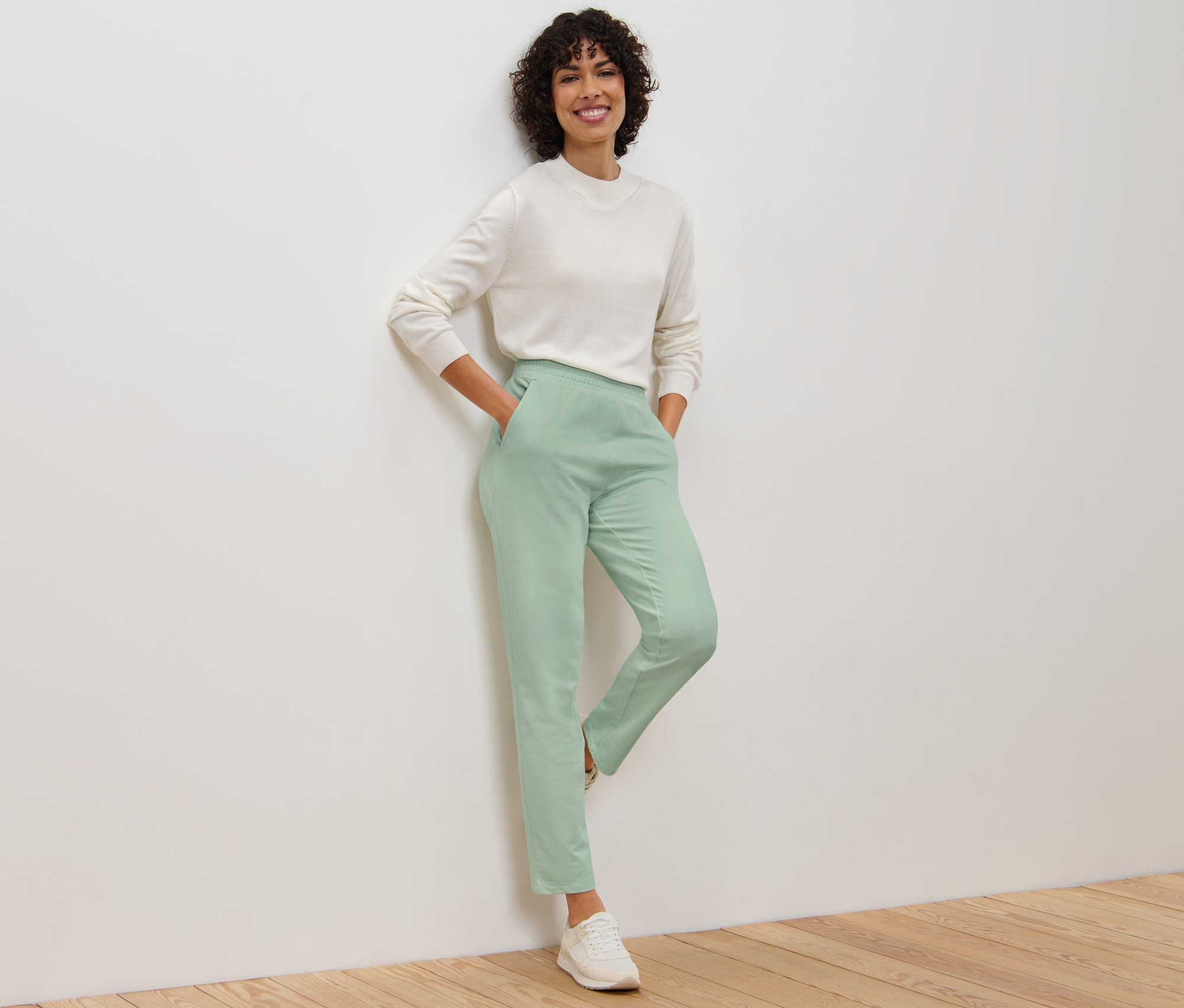 Femme appuyée contre un mur portant un pantalon de jogging et un pull.