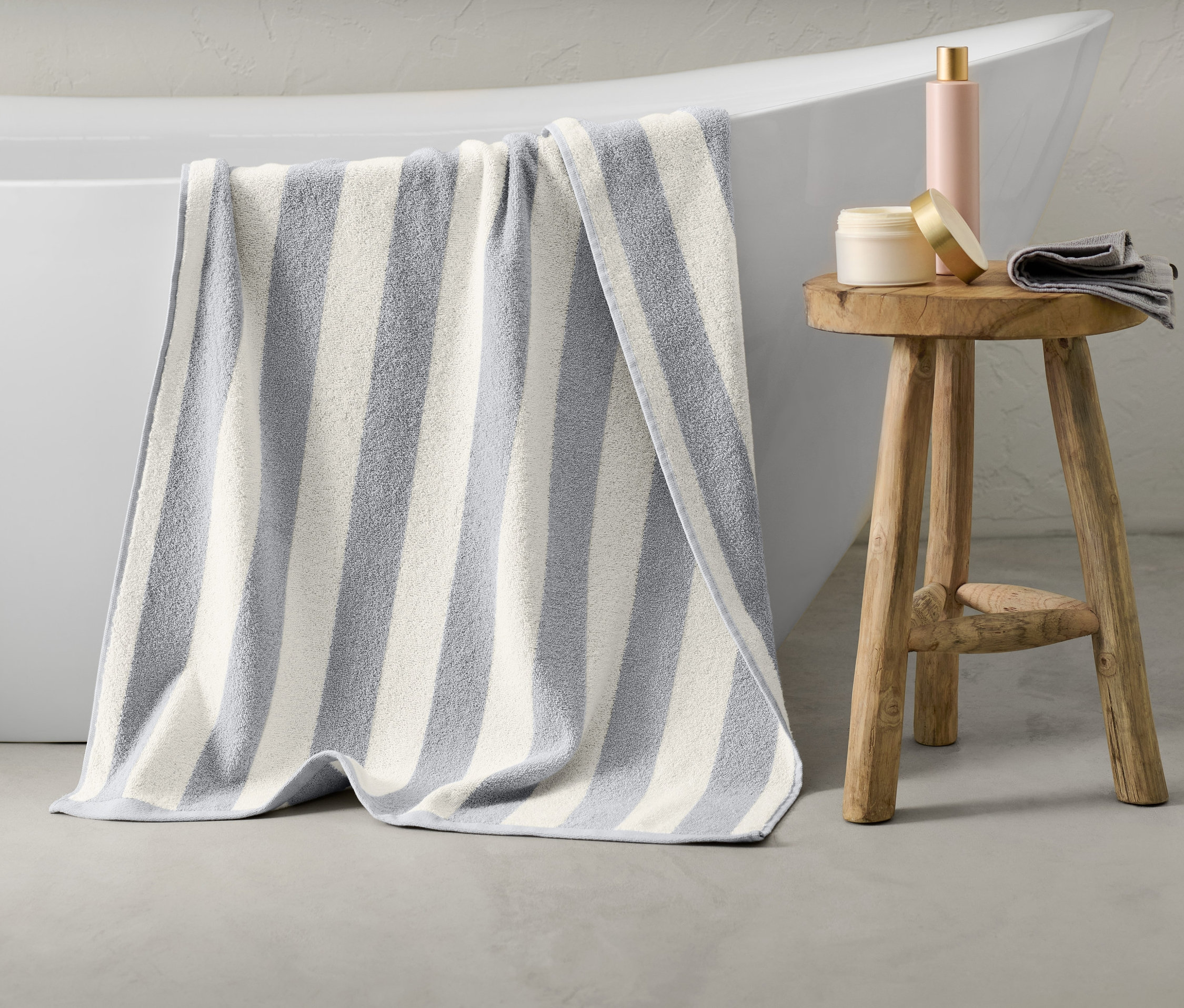 Un drap de bain rayé gris est suspendu au bord d'une baignoire blanche.
