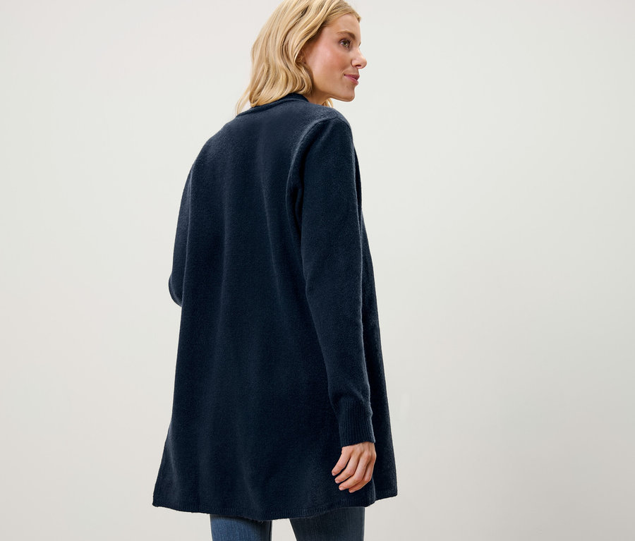 Blonde portant un jean et un cardigan long ouvert regardant vers la droite.