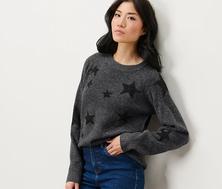 Femme posant en pull en maille avec des étoiles et un jean.
