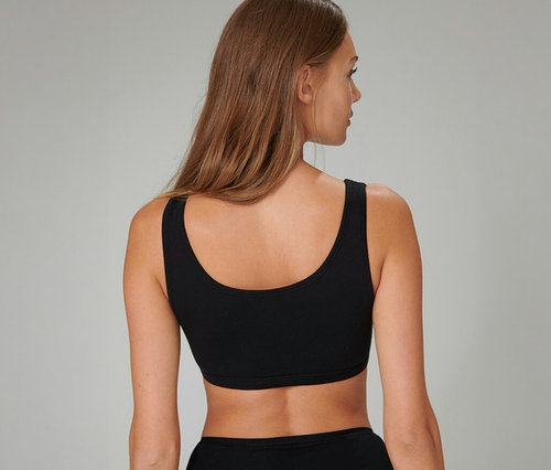 Femme de dos aux longs cheveux bruns, portant une brassière SCHIESSER noire et une culotte noire.