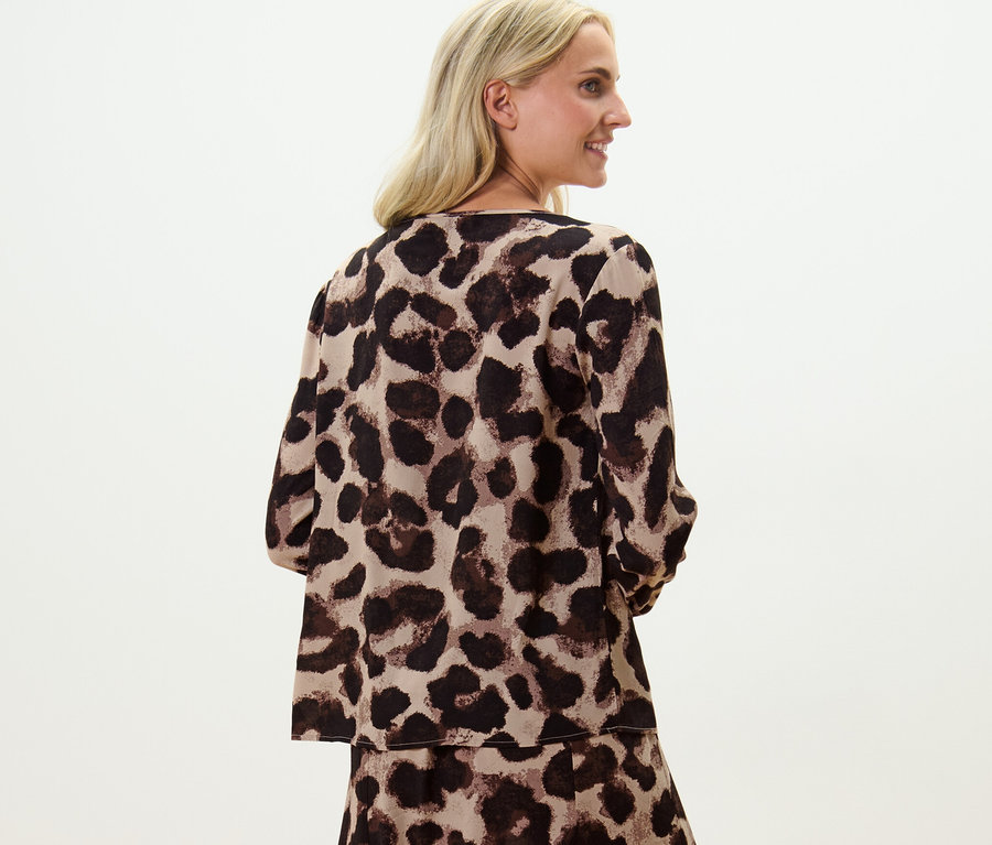 Une femme blonde pose dans une blouse imprimée.
