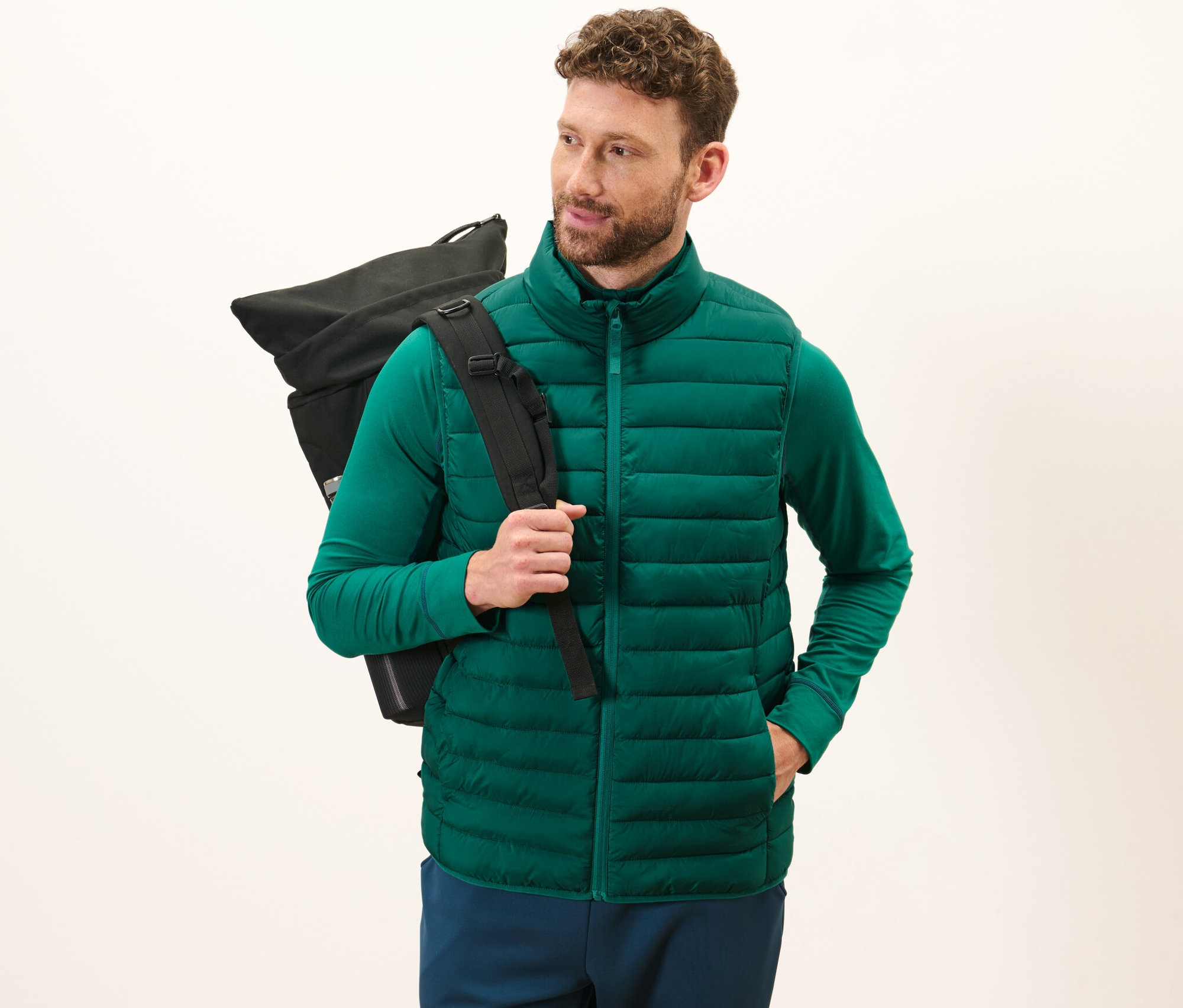 Un homme porte un gilet sans manches matelassé à ranger vert et un sac à dos noir.