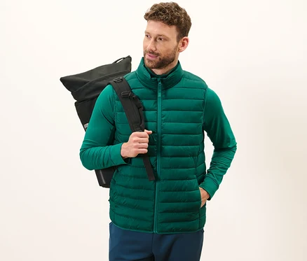 Un homme porte un gilet sans manches matelassé à ranger vert et un sac à dos noir.
