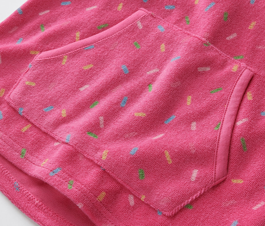 Gros plan sur un poncho en tissu éponge rose pour enfant avec une poche et des motifs colorés.