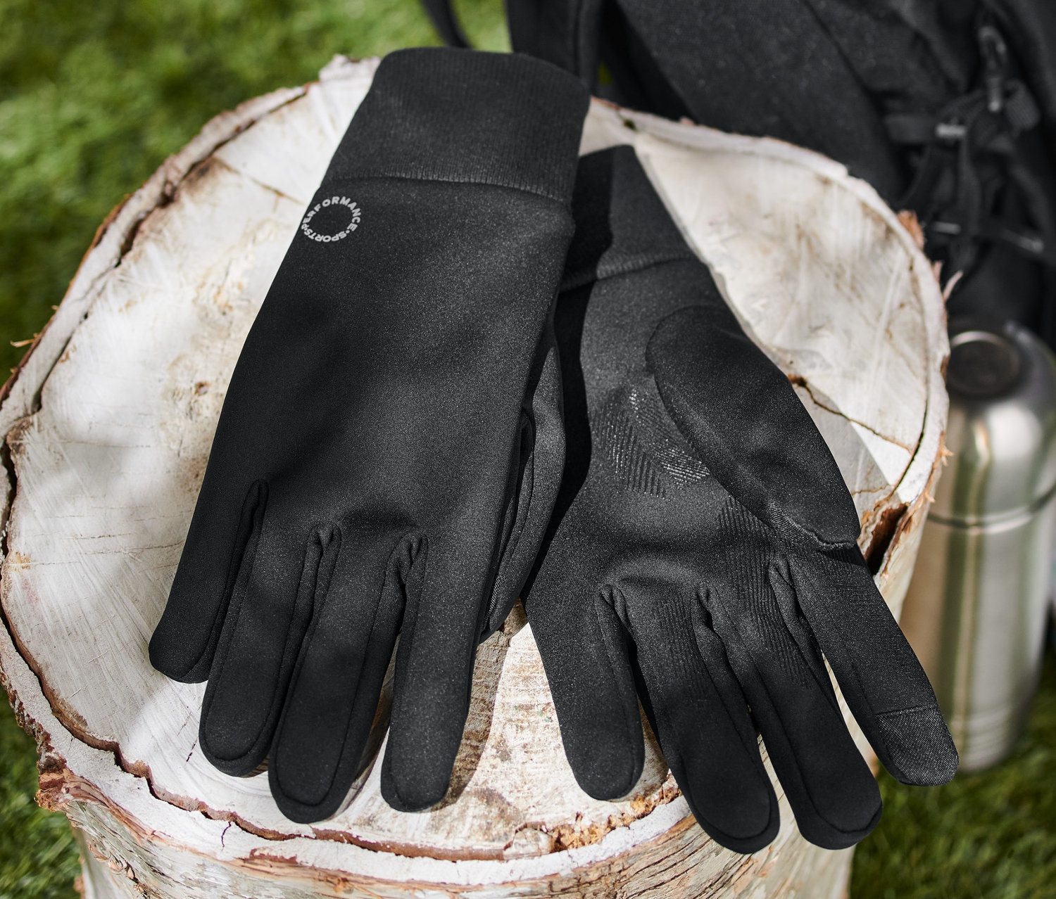 Des gants coupe-vent noirs sont posés sur une souche d'arbre à côté d'une thermos, d'une carte et d'un sac à dos.