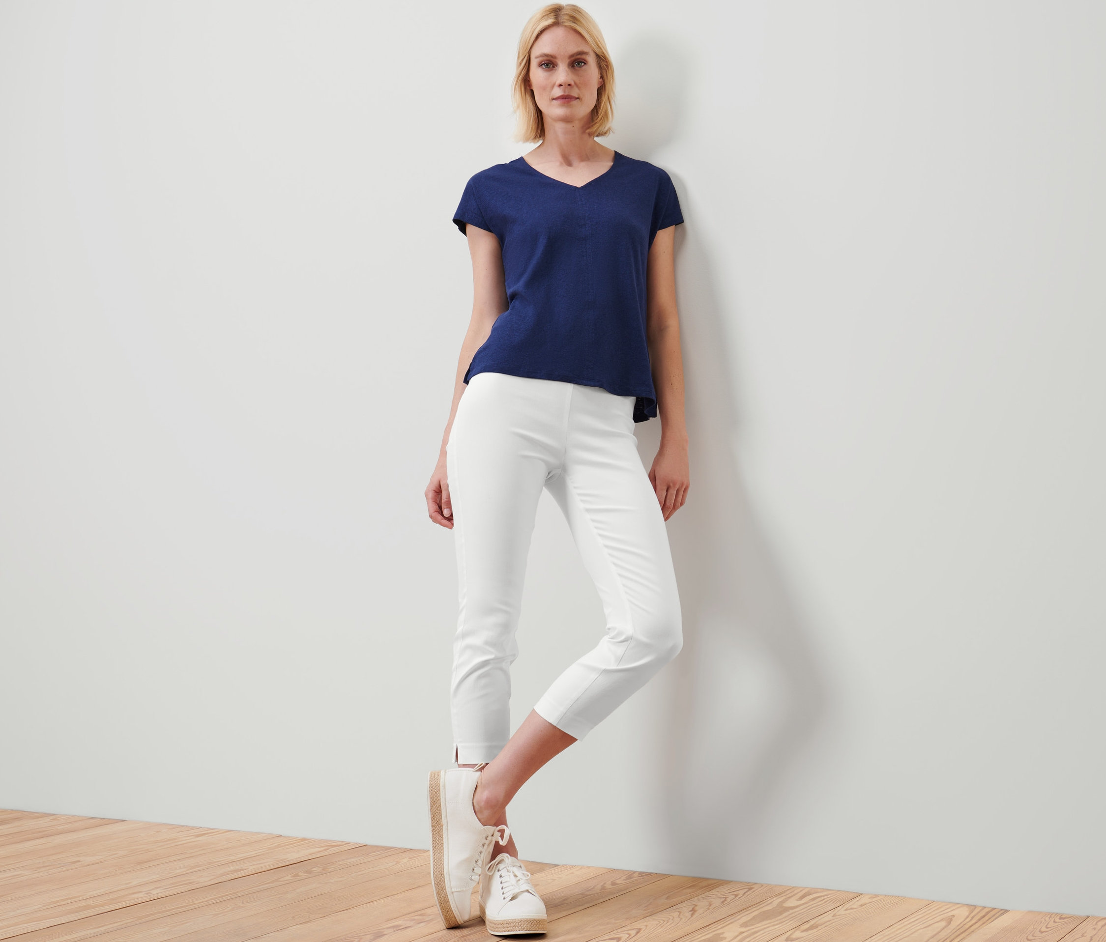 Femme posant dans un haut bleu et un pantalon stretch 7/8 blanc.