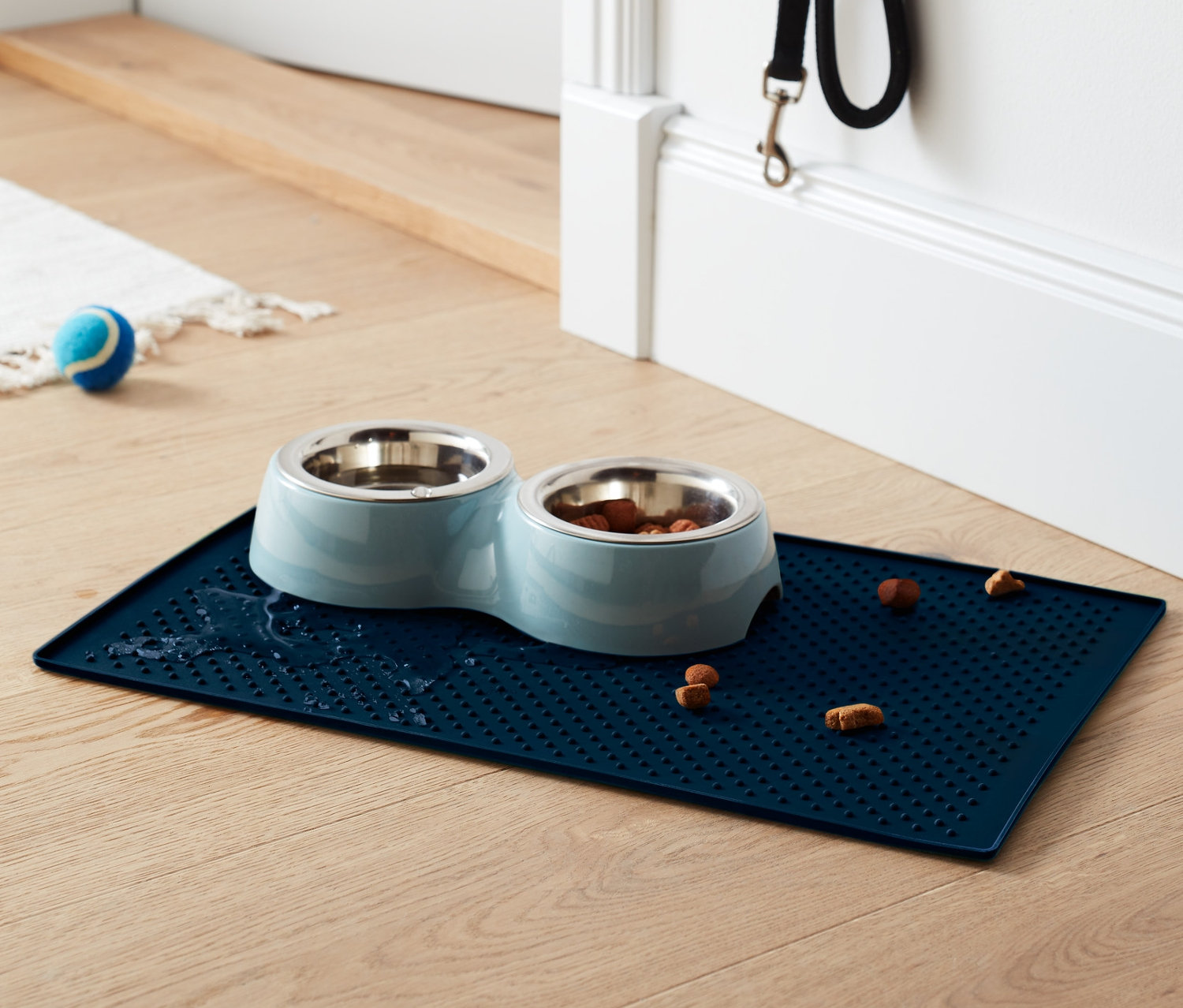 Un dessous de gamelle bleu avec deux gamelles en inox dont une avec de la nourriture sur un plancher en bois.