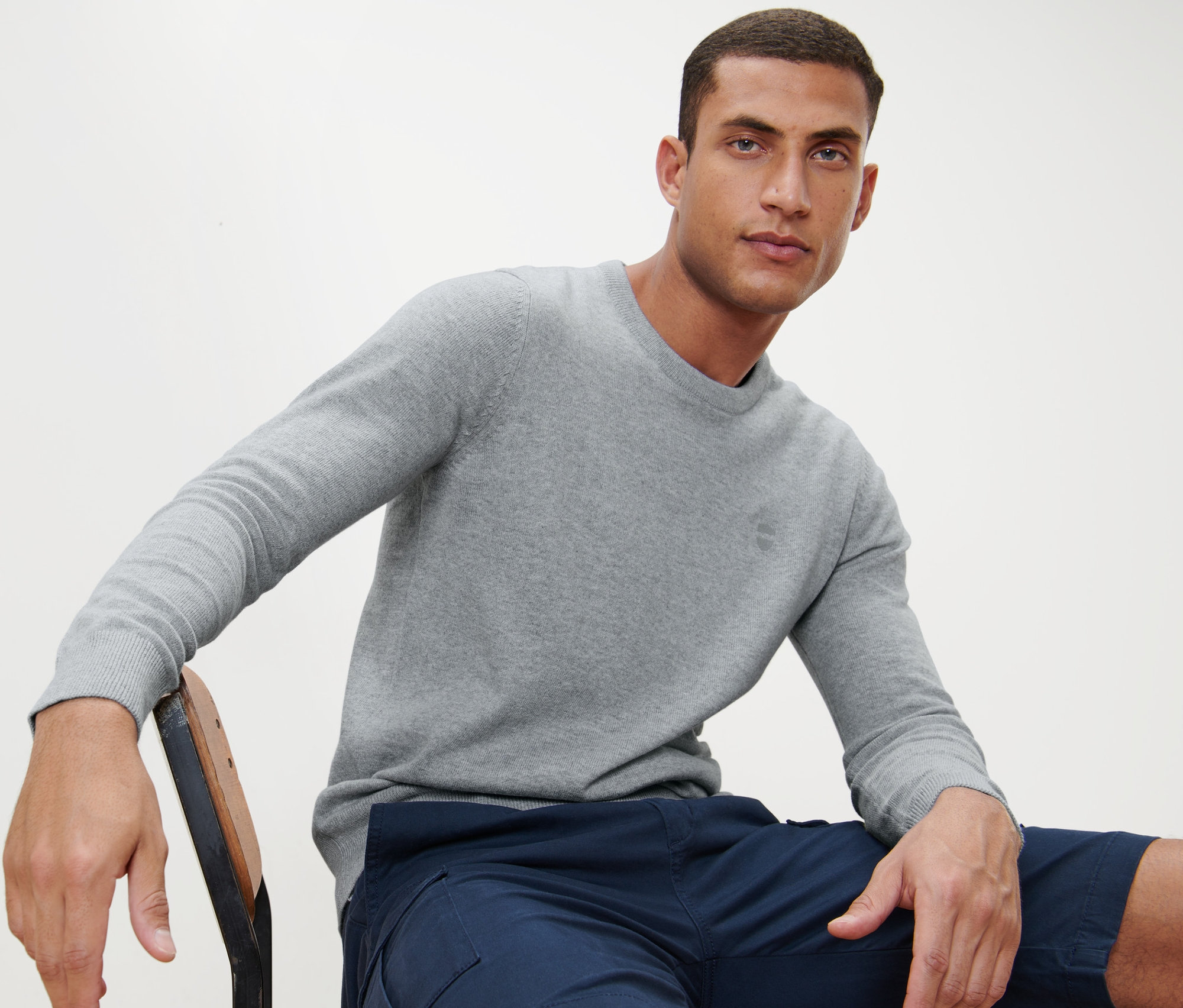 Un homme est assis sur une chaise et porte un pull gris à encolure ronde.