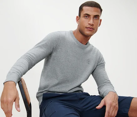 Un homme est assis sur une chaise et porte un pull gris à encolure ronde.