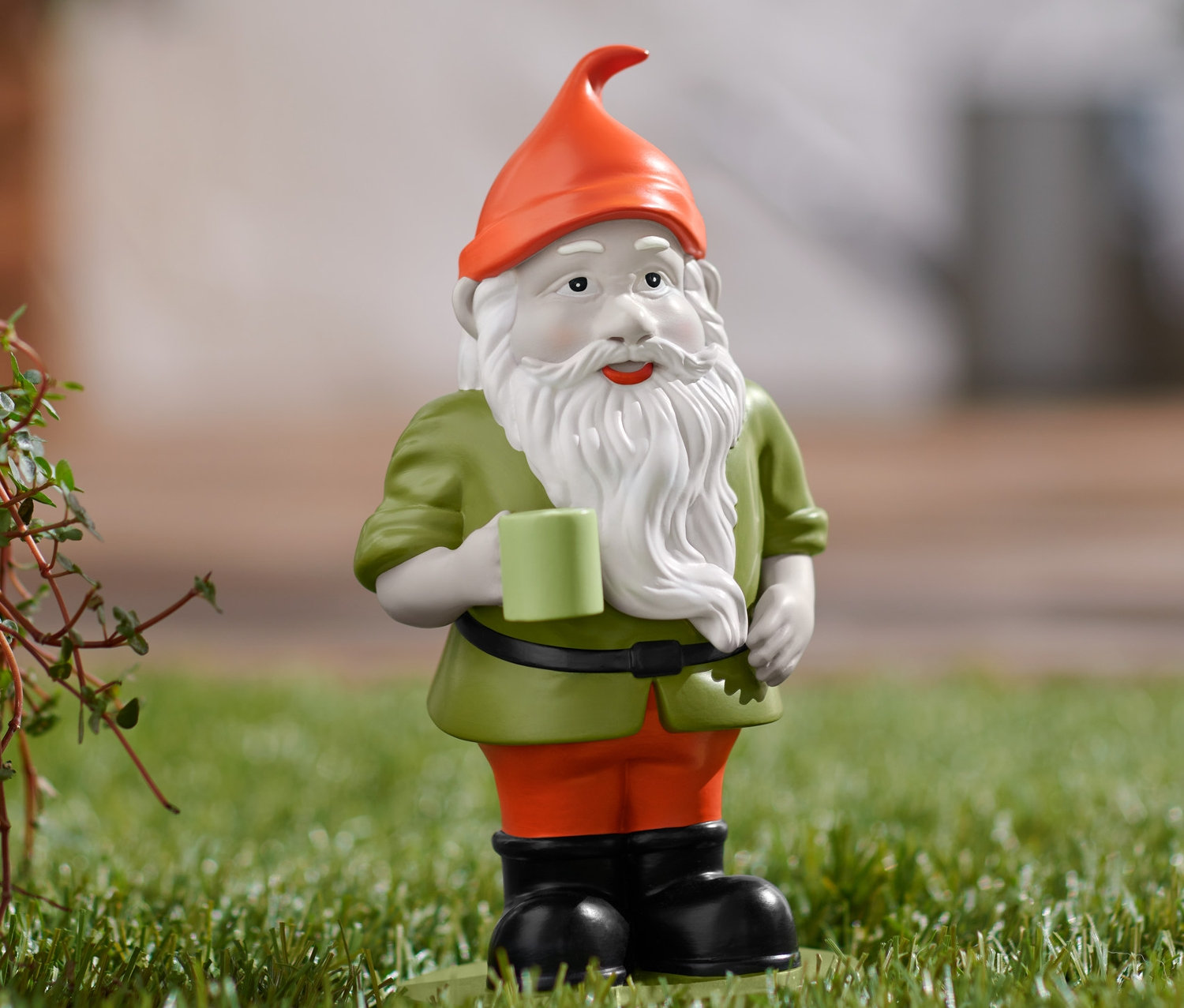 Un nain de jardin se tient sur la pelouse et tient une tasse.
