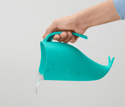 Une main tient un gobelet lave-cheveux pour enfant bleu-vert en forme de baleine, duquel de l'eau coule.
