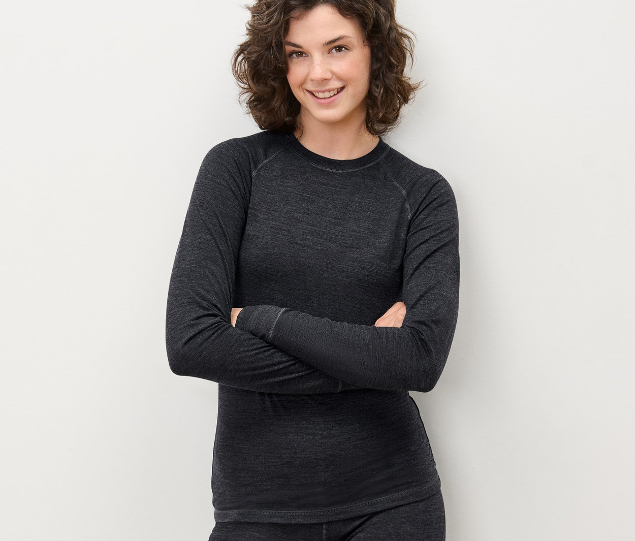 Une femme pose, les bras croisés, portant un t-shirt technique gris avec de la laine certifiée RWS et un pantalon.