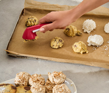 Une femme utilise une portionneuse de biscuits pour déposer de la pâte sur une plaque à pâtisserie.