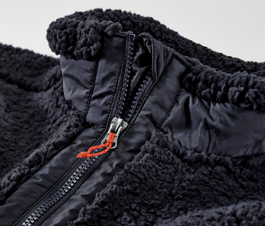 Gros plan d'un gilet sans manches en peluche teddy ouvert avec une fermeture éclair.