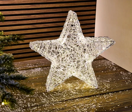 Une étoile décorative d'extérieur à LED illuminée se dresse sur un plancher en bois à côté d'un arbre de Noël.