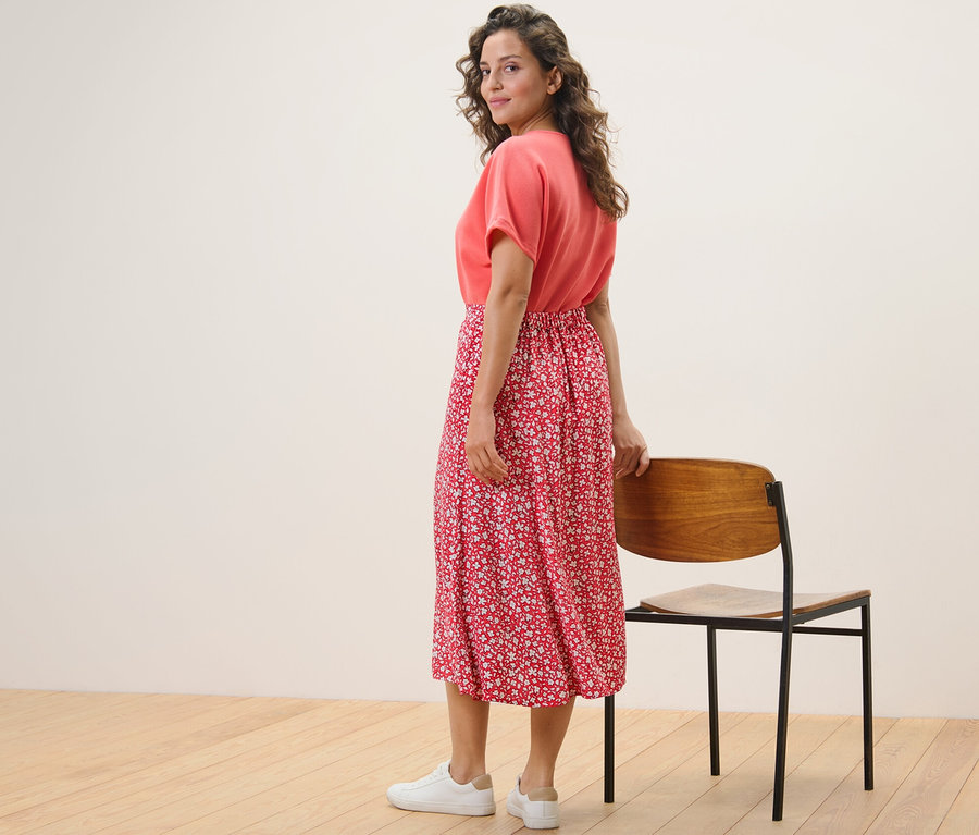 Une femme regardant par-dessus son épaule pose en jupe midi imprimée corail.