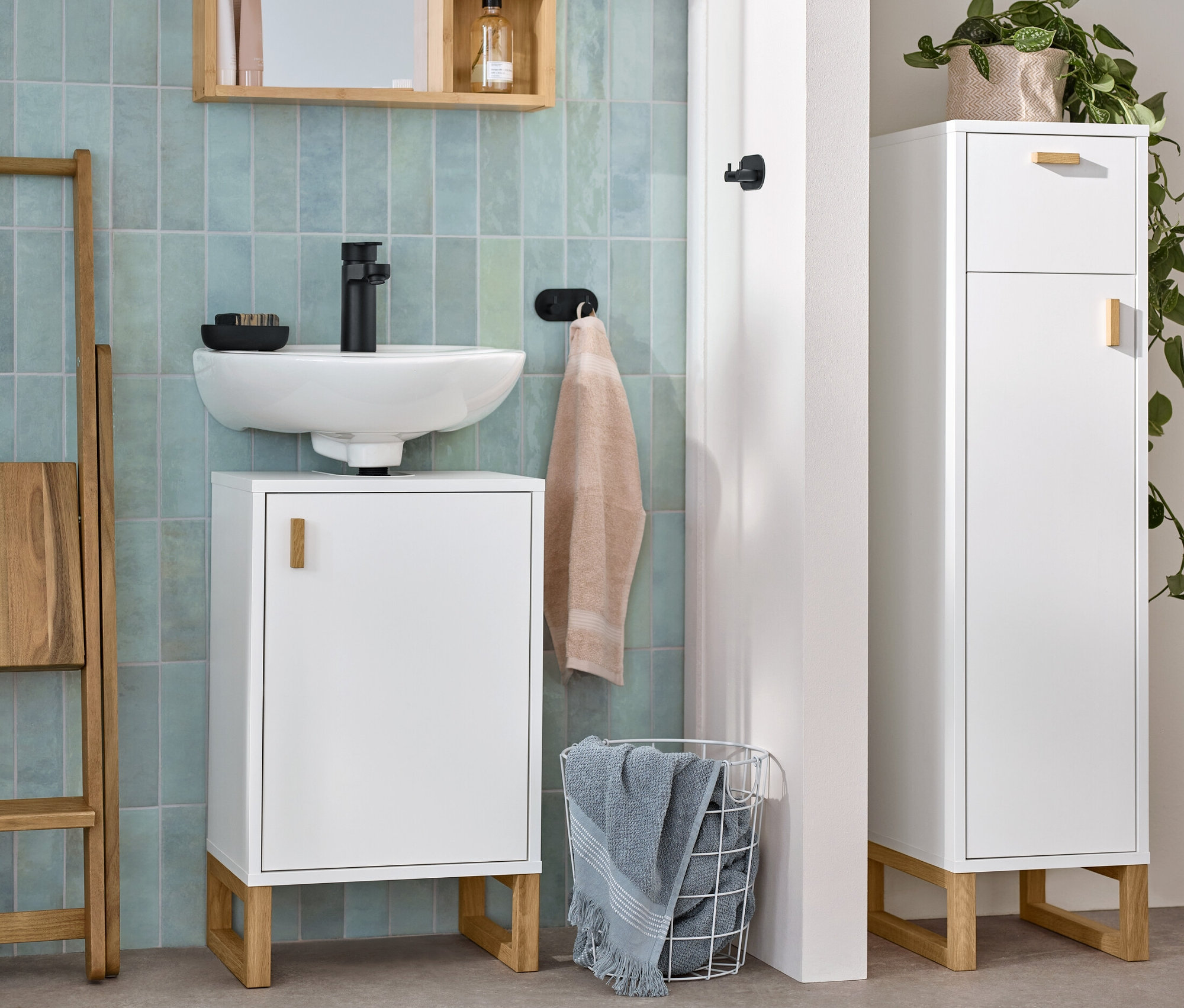 Une salle de bain comprenant un petit meuble sous lavabo avec porte, une armoire d'appoint de salle de bain étroite avec tiroir et porte, et un miroir avec étagères.