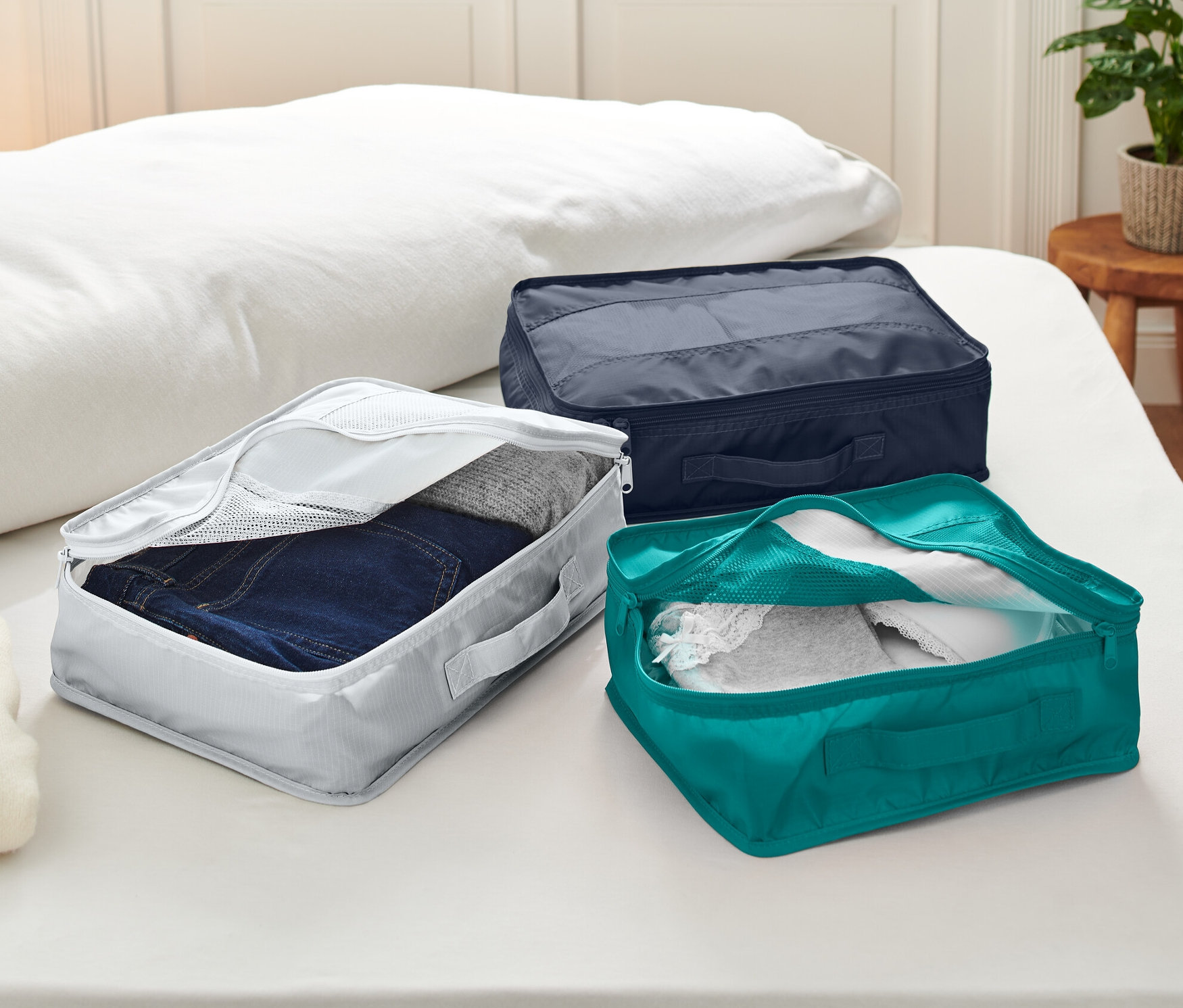 Trois sacs de rangement de voyage posés sur un lit.