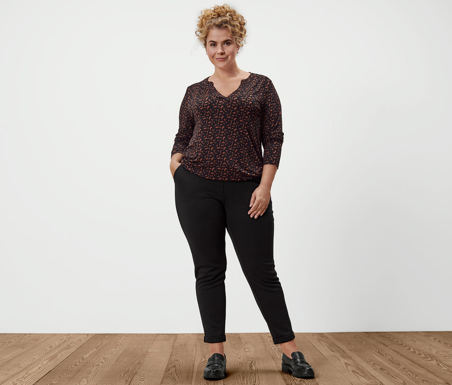 Une femme pose en pantalon de jogging, loafers en cuir et blouse imprimée.