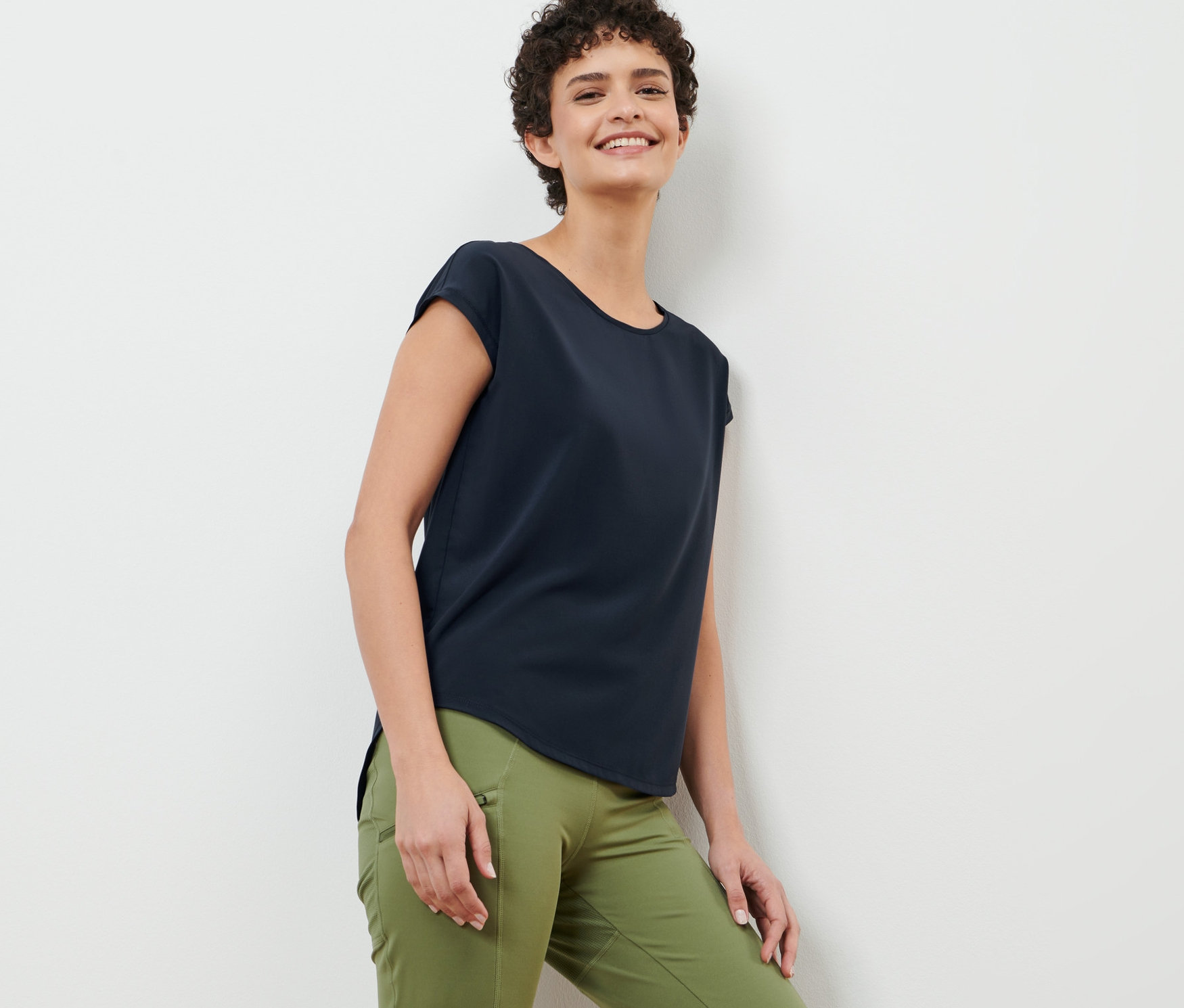 Femme appuyée contre un mur portant un t-shirt de sport bleu foncé.