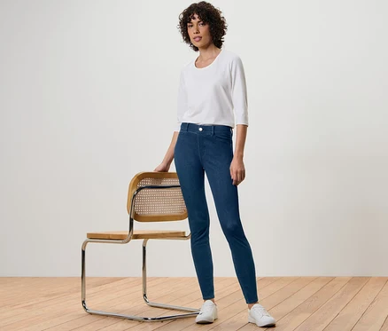 Femme posant à côté d'une chaise portant un jegging, un chemisier blanc et des baskets.