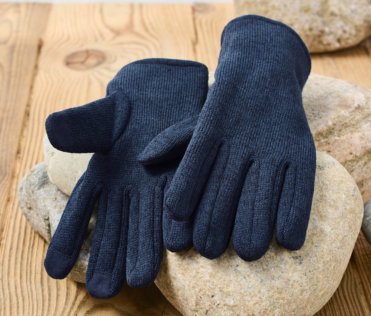 Des gants en polaire tricotée bleu foncé reposent sur des pierres sur une surface en bois.
