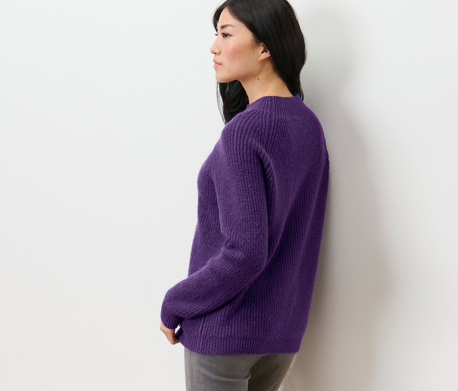 Vue latérale d'une femme aux cheveux foncés portant un pull violet à col droit en grosse maille.