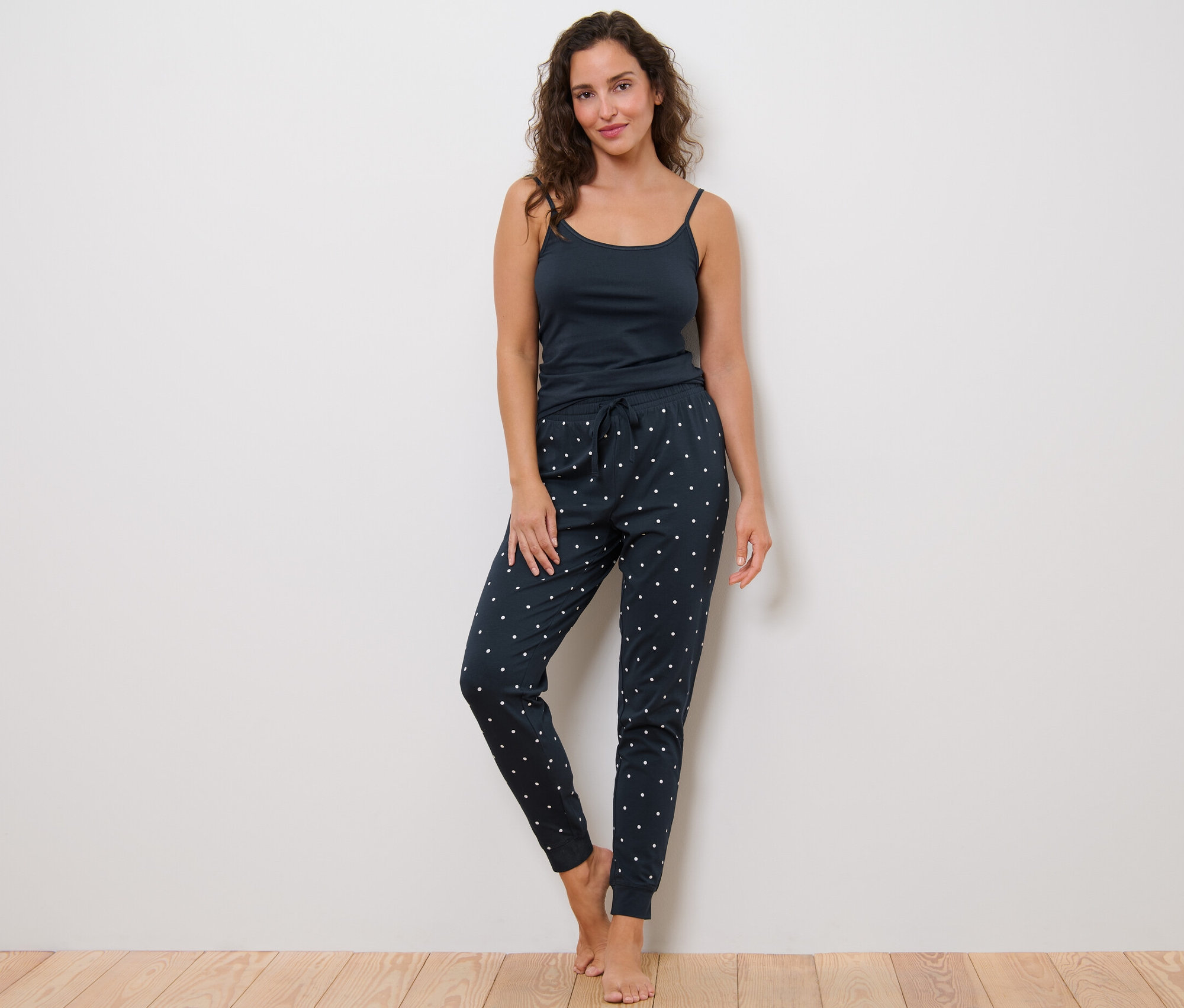 Femme debout portant un pantalon de pyjama à pois et un débardeur.