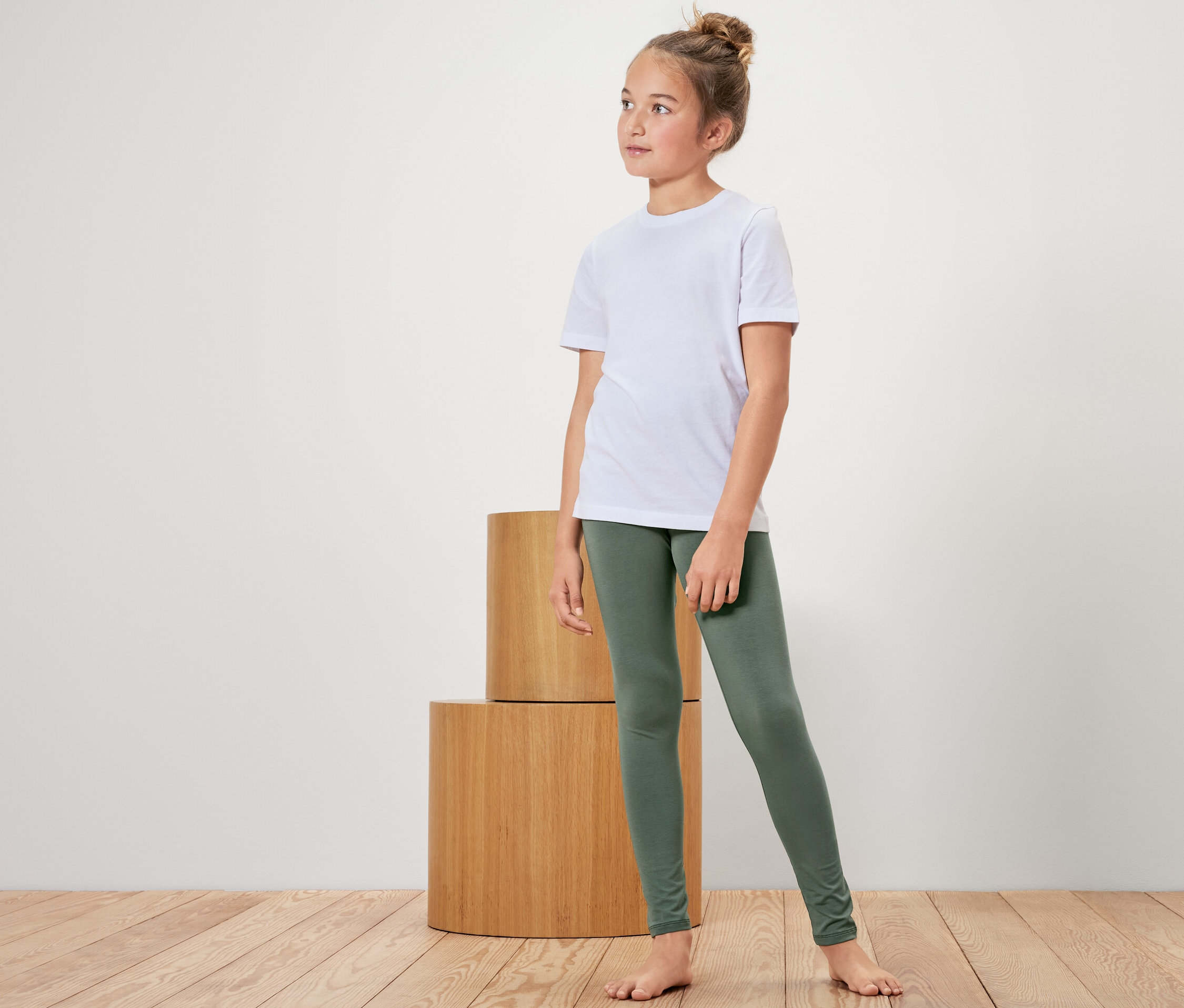 Une fille portant un t-shirt blanc et un legging vert se tient à côté de cylindres en bois.