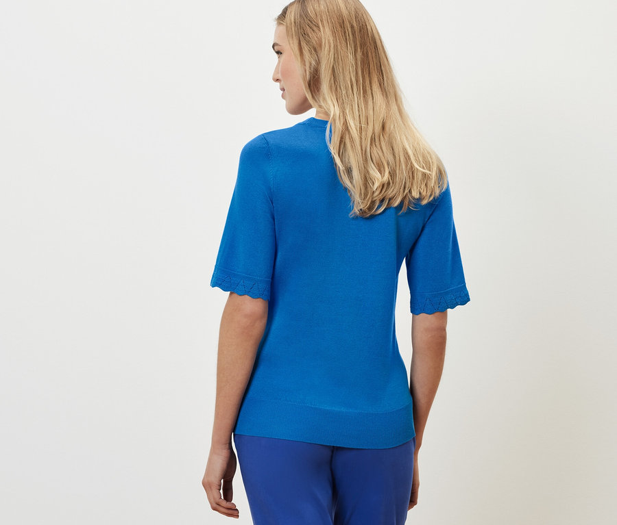 Une femme blonde, vue de dos, porte un pull en maille fine bleu cobalt et un pantalon bleu.